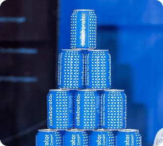 Pyramid stack of blue Collaborator-branded cans arranged in multiple tiers, creating an eye-catching display against a blue background